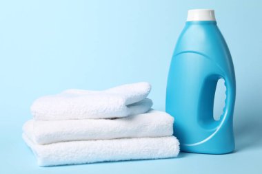 Bir şişe yumuşatıcı ve açık mavi arka planda havlular.