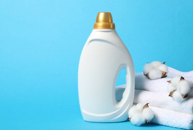 Bir şişe yumuşatıcı, pamuk çiçekleri ve açık mavi arka planda havlular, metin için alan