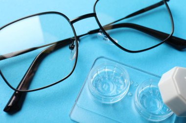 Açık mavi arkaplanda kontak lensler ve gözlükler, yukarıda görünüm