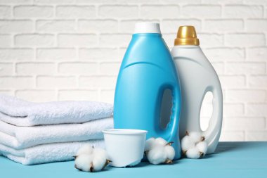 Beyaz tuğla duvara karşı açık mavi masada yumuşatıcı, havlu ve pamuk çiçekleri.