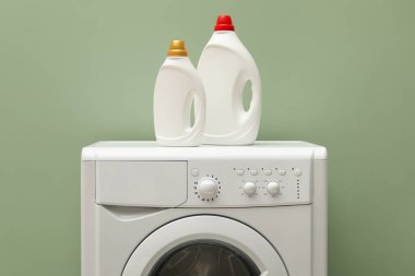 Çamaşır makinesinin üzerinde soluk yeşil duvarın yanında yumuşatıcı şişeler.