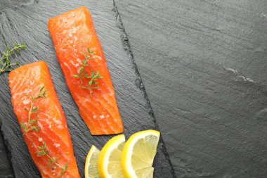 Deniz ürünleri. Somon fileto parçaları, kekik ve limon dilimleri siyah desenli masa, üst manzara. Metin için boşluk