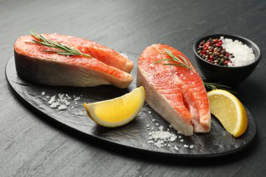 Deniz ürünleri. Siyah desenli masada somon biftekleri, baharatlar ve limon dilimleri, yakın plan.