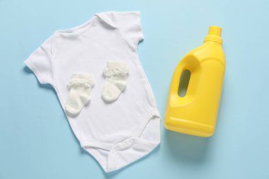 Bir şişe yumuşatıcı ve açık mavi arka planda bebek kıyafetleri.