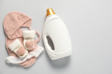 Bir şişe yumuşatıcı ve açık gri arka planda bebek kıyafetleri. Metin için boşluk