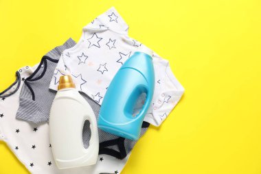 Sarı arka planda yumuşatıcı ve bebek kıyafetleri var. Metin için boşluk