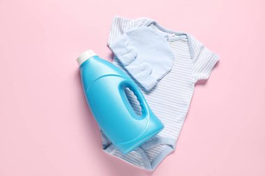 Bir şişe yumuşatıcı ve pembe arka planda bebek kıyafetleri.