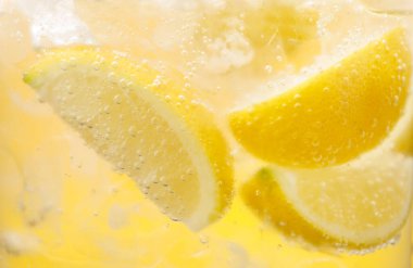 Sarı arka planda limon dilimleri ve buzla soda tazeleniyor. Yakın plan.