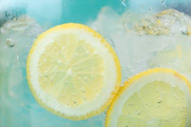 Açık mavi arka planda limon dilimleri ve buzla soda tazeleniyor. Yakın plan.