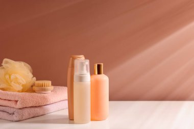 Açık kahverengi duvarın yanındaki beyaz masada farklı banyo ürünleri. Metin için boşluk