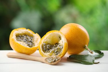 Olgun tutku meyveleri, yeşil yapraklar ve tohumlar beyaz ahşap masa üzerinde, yakın plan.