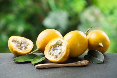 Olgun tutku meyveleri, yeşil yapraklar ve tohumlar dışarıda, siyah masada.