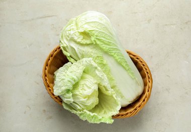 Hasır sepetin içinde taze Çin lahanaları açık gri masada, üst tarafta.