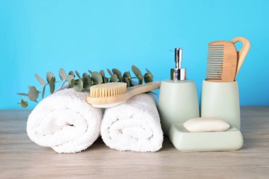 Farklı banyo aksesuarları ve okaliptüs dalları açık mavi arkaplana karşı ahşap masa üzerinde, yakın plan