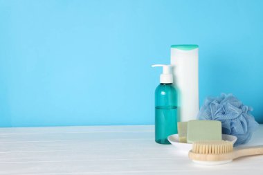 Açık mavi arka planda beyaz ahşap masada farklı banyo aksesuarları, yakın plan. Metin için boşluk