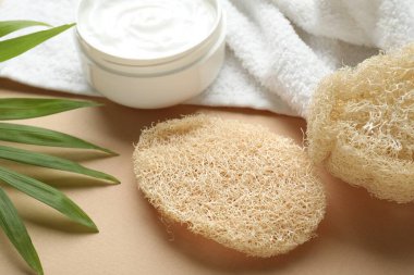 Doğal lif süngeri, kozmetik ürünü, bej arka planda havlu ve yeşil yapraklar, yakın plan.