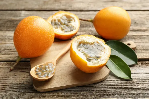 Olgun tutku meyveleri, tohumlar ve yeşil yapraklar ahşap masada, yakın plan.