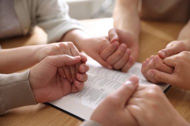 İncilli aile ahşap masada dua ediyor, yakın plan.