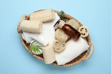 Doğal lif süngerleri, havlular, kozmetik ürünleri ve açık mavi arka plan sepetinde çiçek dekoru.