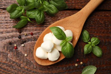 Kaşıkta mozarella peyniri topları, ahşap masada karabiber ve fesleğen.