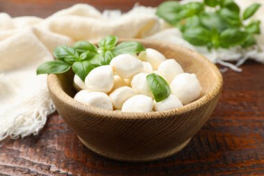 Lezzetli mozzarella peynir topları kasede ve fesleğen ahşap masada, yakın plan.