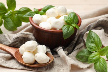 Lezzetli mozzarella peynir topları kasede, fesleğen ve kaşık açık ahşap masada, yakın plan.