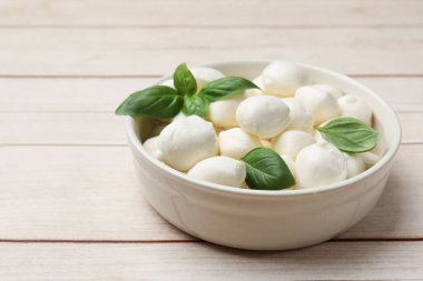 Lezzetli mozzarella peyniri topları kasede ve fesleğen açık ahşap masada, yakın plan. Metin için boşluk