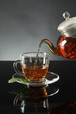 Koyu ayna masasında çaydanlıktan fincana taze demlenmiş çay dökülüyor.