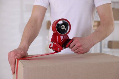 Karton kutuyu kapalı bir yere kapatmak için yapıştırıcılı bant kullanan bir adam.