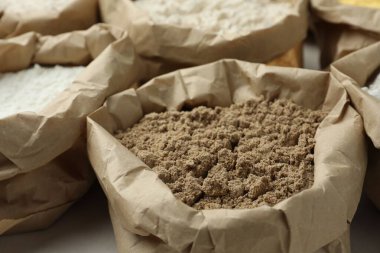 Beyaz masadaki kağıt torbalarda farklı türde un, yakın plan.