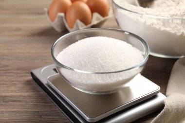 Dijital mutfak terazisi, bir kase şeker ve ahşap masa üzerindeki diğer ürünler, yakın plan.