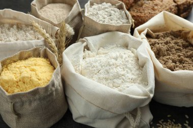 Gri masadaki çantalarda farklı tipte un, yakın plan.