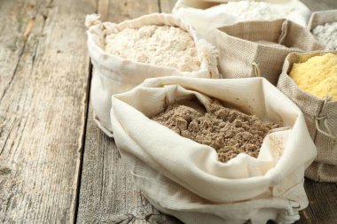 Tahta masadaki poşetlerdeki farklı un türleri, yakın plan. Metin için boşluk