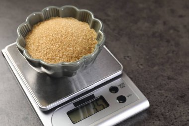 Dijital mutfak terazisi ve gri masada bir kase kahverengi şeker, yakın plan. Metin için boşluk