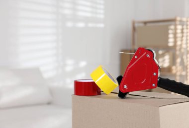 Kapalı alandaki karton kutunun üzerinde yapışkan bant ruloları olan bir dağıtıcı.