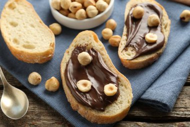 Çikolata sürülmüş ekmek dilimleri ve ahşap masada fındıklar, yakın plan.