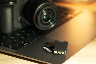 SD hafıza kartları, dizüstü bilgisayar ve fotoğraf makinesi ahşap masada, yakın plan.