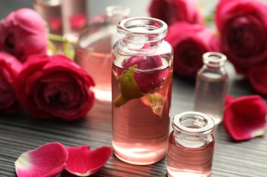 Aromatik esanslı parfüm şişelerini aç ve gri ahşap masada güller, yakın plan.