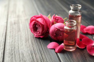 Gri ahşap masada aromatik esanslı yağlar ve güllerle parfüm şişelerini açın. Yakın plan. Metin için boşluk