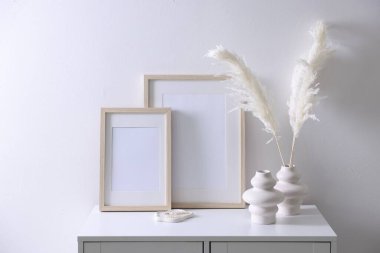 Beyaz duvarın yanındaki dolapta boş resim çerçeveleri ve şık ev dekorasyonu