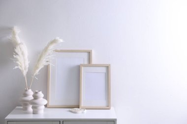 Beyaz duvarın yanındaki dolapta boş resim çerçeveleri ve şık ev dekorasyonu, metin için boşluk