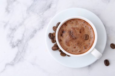 Bardakta romatik kahve, beyaz mermer masada fasulye ve çay tabağı, üst manzara. Metin için boşluk