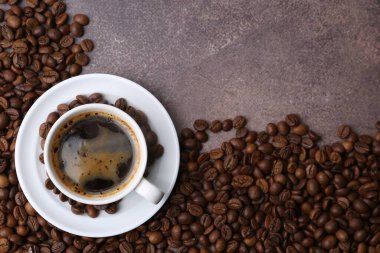 Aromatik kahve fincanda, fincan tabağı ve kahve çekirdekleri kahverengi desenli masada, düz yerde. Metin için boşluk