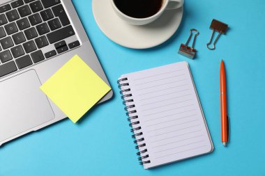 Not defteri, yapışkan not, kalem, cilt klipleri, açık mavi zemin üzerinde kahve ve dizüstü bilgisayar, düz uzanma