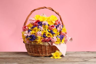 Ahşap masada pembe arka planda güzel çiçeklerle dolu bir sepet.