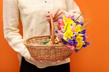 Turuncu arka planda güzel çiçekli hasır sepet tutan kadın, yakın plan.