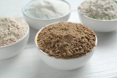 Beyaz ahşap masadaki kaselerdeki farklı un türleri, yakın plan.