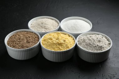 Siyah desenli masa üzerindeki kaselerde farklı un türleri, yakın plan.