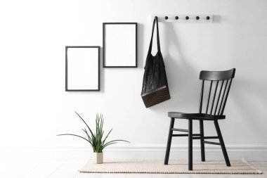 Beyaz duvarda boş resim çerçeveleri, sicim torbası, sandalye ve ev bitkisi