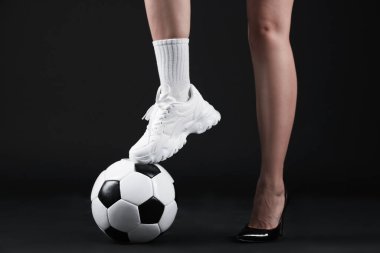 Arka planda futbol topu olan yüksek topuklu ayakkabılı ve spor ayakkabılı bir kadın.